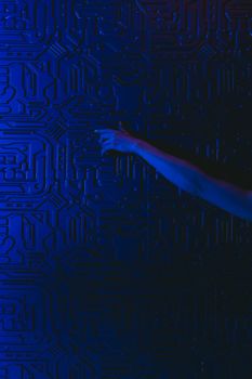 A hand reaches out to touch a futuristic blue circuit patterned wall with dramatic lighting.