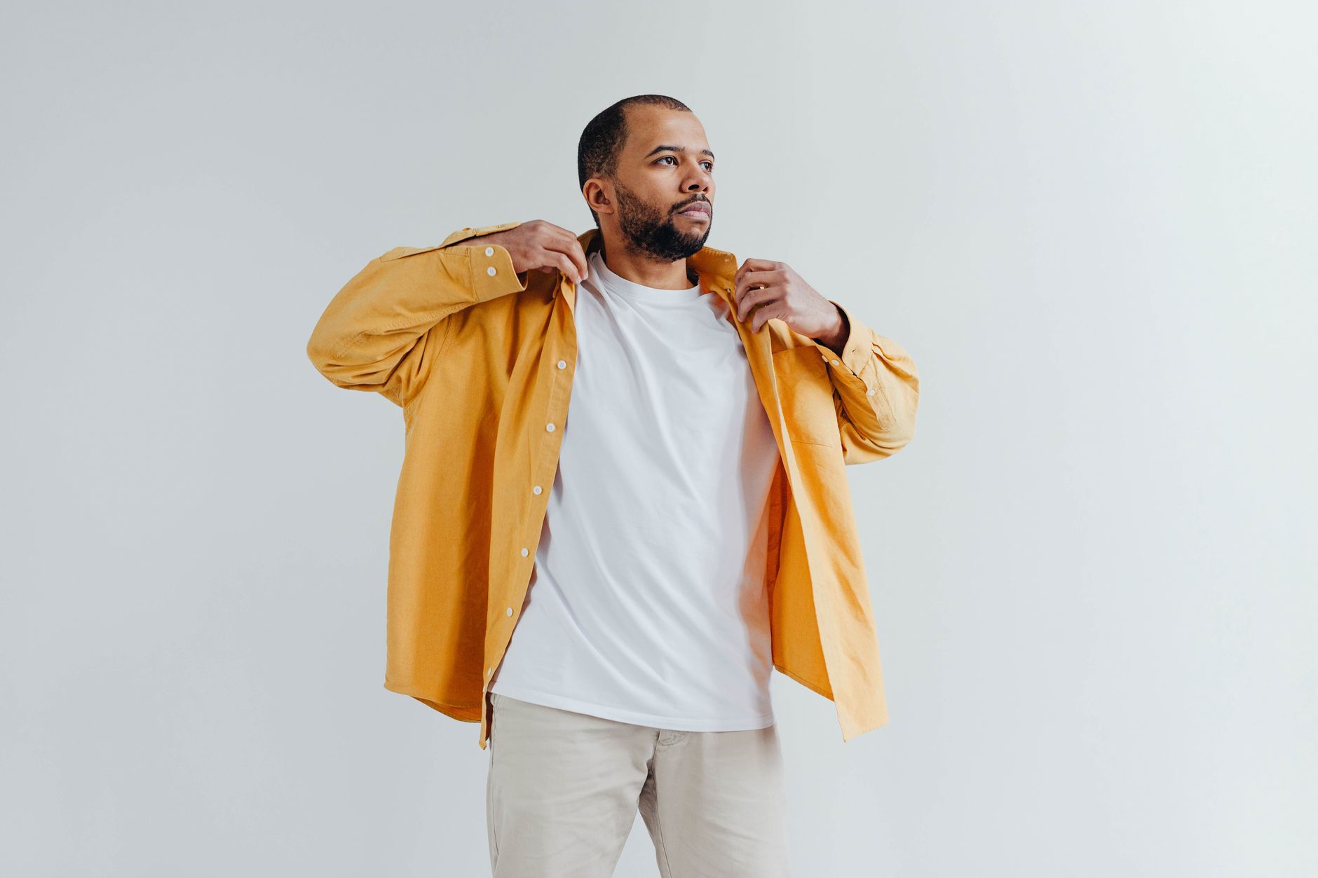 Fashionable man wearing a yellow shirt and white t-shirt against a minimalistic white backdrop.