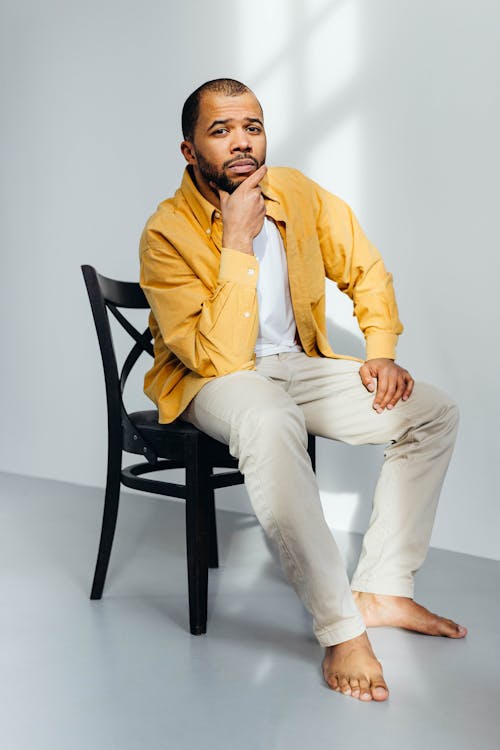 Man in Yellow Long Sleeve Shirt and Beige Pants Sitting on Black Wooden Chair