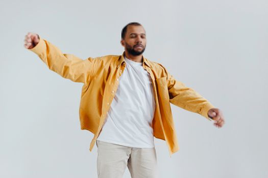 Man in yellow jacket poses casually with arms outstretched against white background.