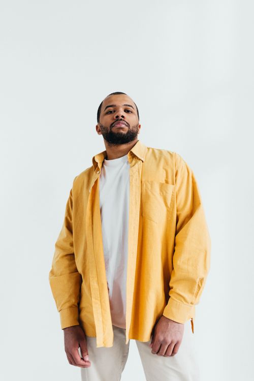 Free African American man in a yellow shirt, looking confident, studio setting. Stock Photo
