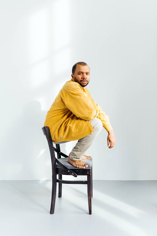 Man in Yellow Long Sleeve Shirt Sitting on Black Wooden Chair
