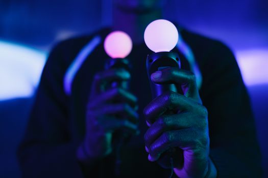 Close-up of hands holding virtual reality controllers in a neon-lit setting, emphasizing technology and gaming.