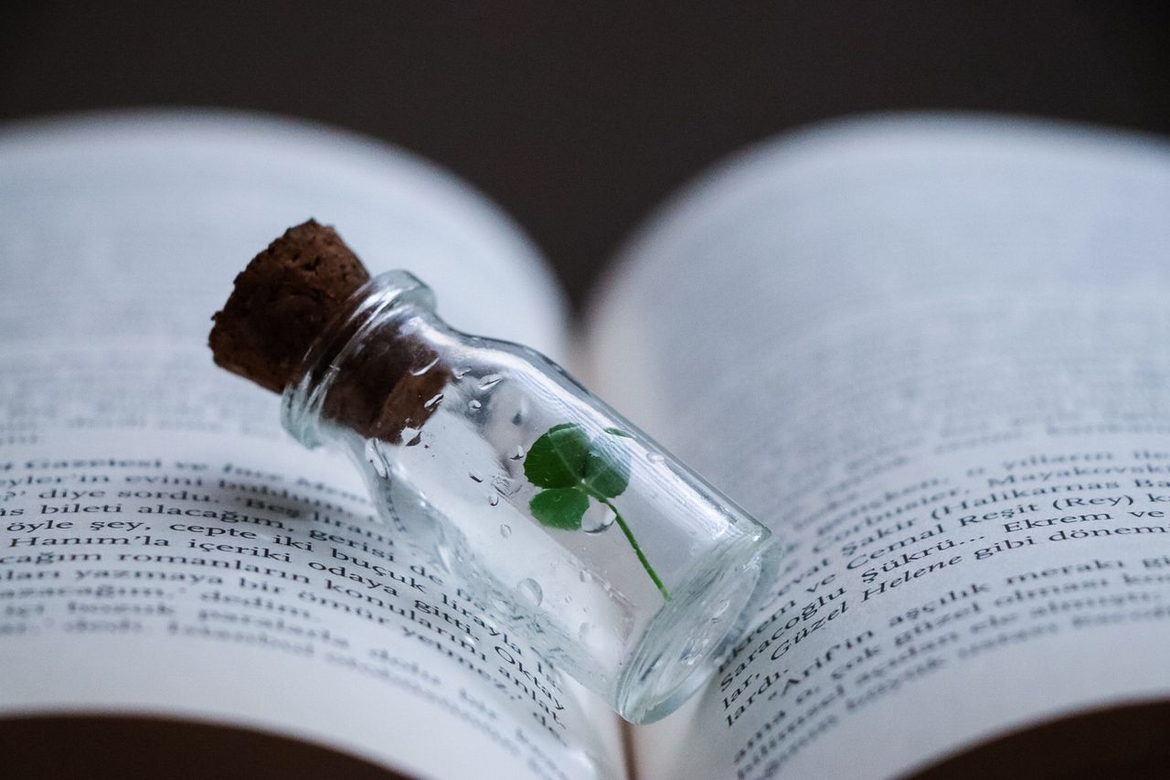 a small clover sealed in a corked glass vial resting on the pages of a