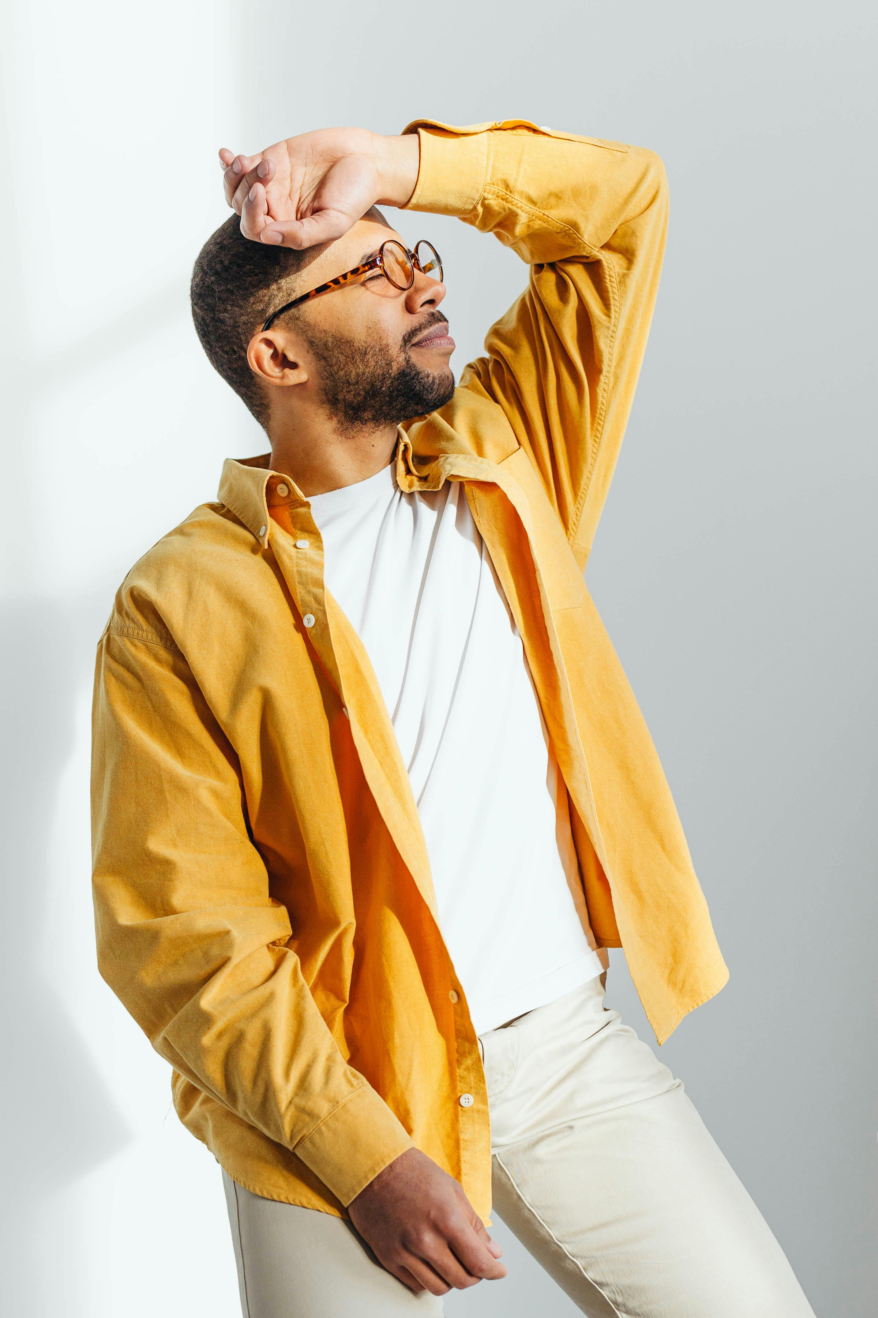 African American man striking a pose against a bright studio background wearing a mustard shirt.