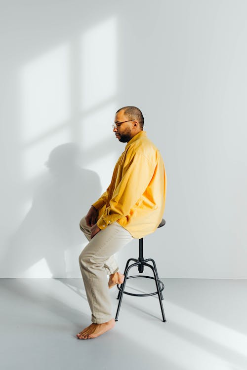 Barefoot Man Wearing Yellow Long Sleeves while Sitting on the Black Chair
