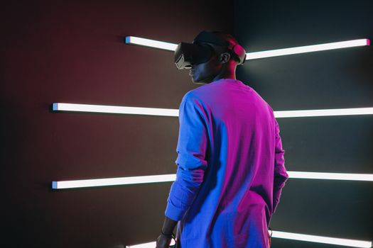 Man using VR headset in a room with vibrant neon lights and modern technology ambiance.