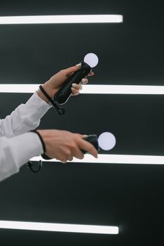 Close-up of hands holding VR motion controllers against bright neon stripes, symbolizing modern gaming technology.