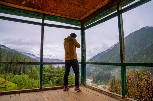 Free A photographer captures a breathtaking mountain view from a wooden structure, surrounded by mist. Stock Photo