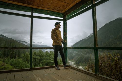 Free A photographer enjoys the serene misty mountain view from a wooden structure in Shallabugh. Stock Photo