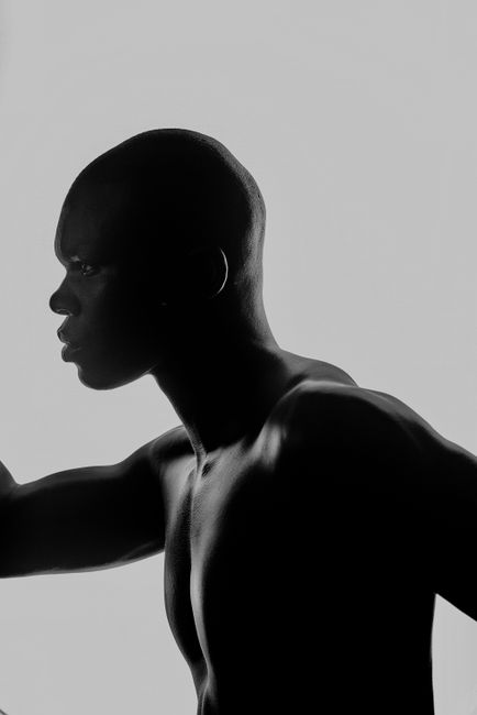 Dramatic black and white profile silhouette of a shirtless man set against a light background.