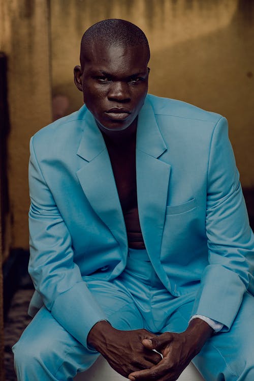 Confident African American male in bright blue suit sitting on pedestal and looking at camera