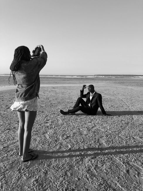 A photographer captures a man's stylish pose on a serene Zanzibar beach in black and white.