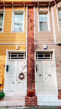 Facade of colorful residential buildings with windows and white doors decorated with vegetation and potted plant located on street of town