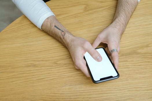 Close-up of hands using a smartphone with a blank screen on a wooden table indoors.