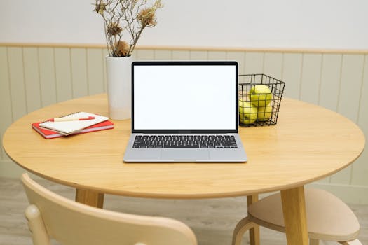 A tidy workspace featuring a laptop, notebooks, and a basket of green apples on a wooden table.