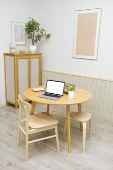 A modern minimalist home office space featuring a round wooden table with a laptop, books, and decor.