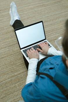 Person working on a laptop while sitting on the floor at home, emphasizing remote work.