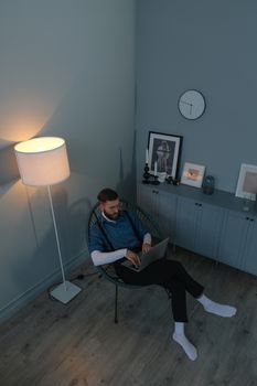 Man sitting in a stylish room reading a laptop, surrounded by modern decor and ambient lighting.
