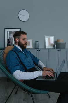 Bearded man with eyeglasses typing on laptop while working remotely from home.