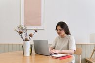 Woman in White Long Sleeve Shirt Using Macbook Air on Brown Wooden Table