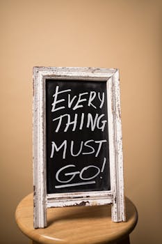 A vintage chalkboard sign displaying the text 'Everything Must Go' placed on a wooden stool against a beige background.