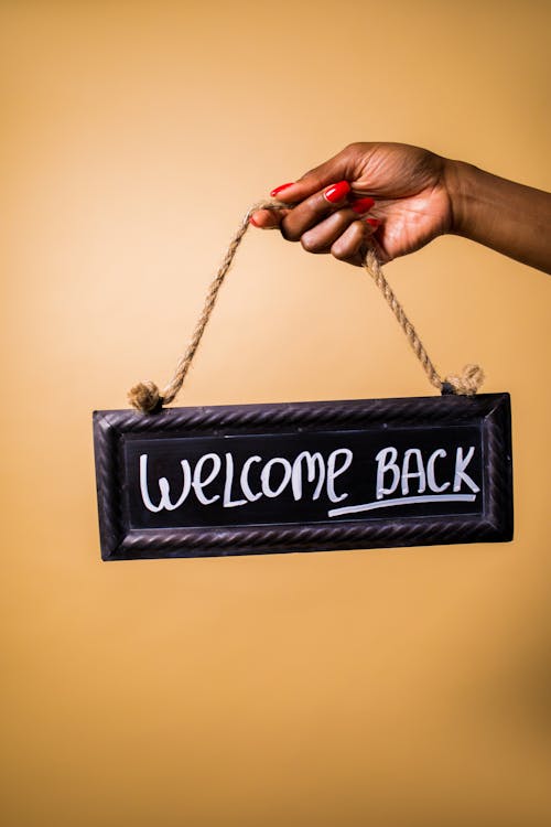 Free Person holding a welcome back sign against a yellow background, offering inviting vibes. Stock Photo