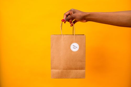 Free A woman's hand holding a brown paper gift bag labeled 'Special Gift' against a vibrant yellow backdrop. Stock Photo