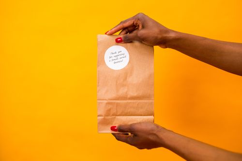 Free Paper bag with a thank you note held by hands against a vibrant yellow background. Stock Photo