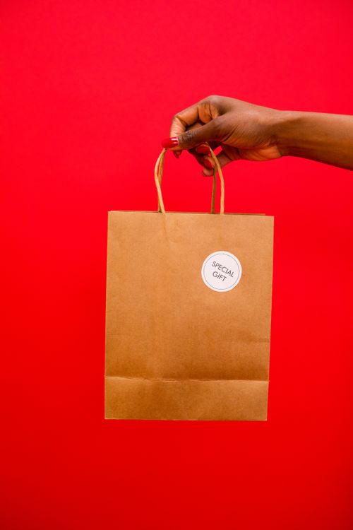 Free A brown paper bag held against a vibrant red background, ideal for gift branding. Stock Photo