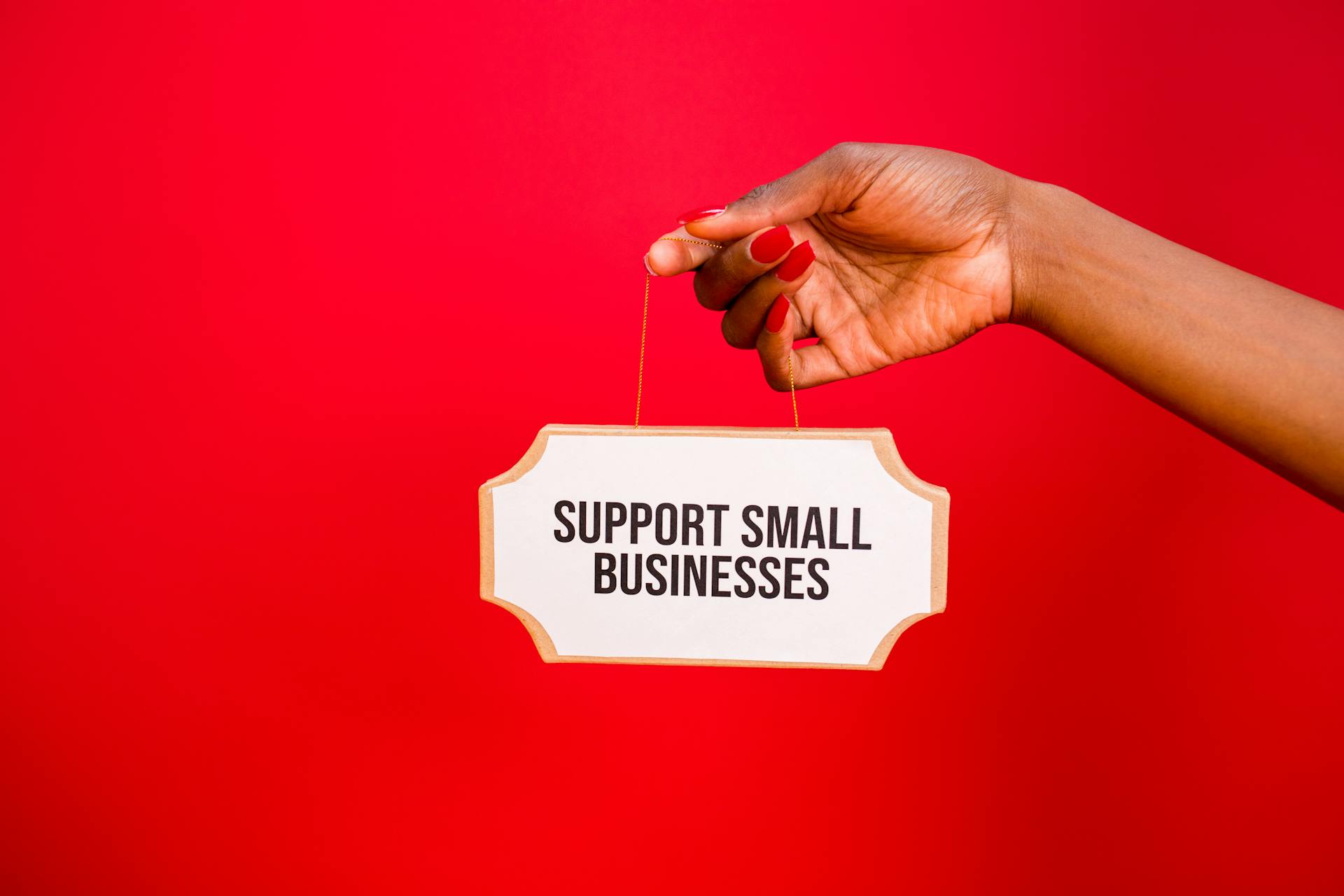 A hand holds a sign that reads 'Support Small Businesses' against a vibrant red background.