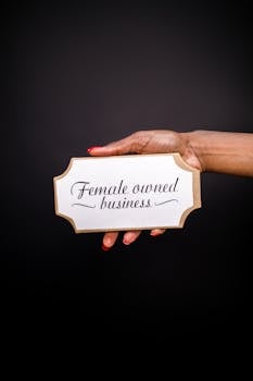 Hand holding a sign with 'Female owned business' on a black background.