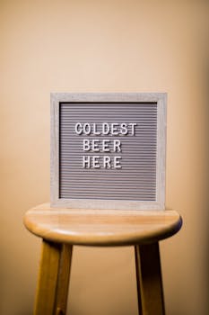 Retro sign displaying 'Coldest Beer Here' on a vintage stool.