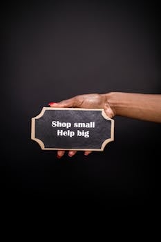 Close-up of a hand holding a 'Shop small, Help big' sign, promoting small business support.