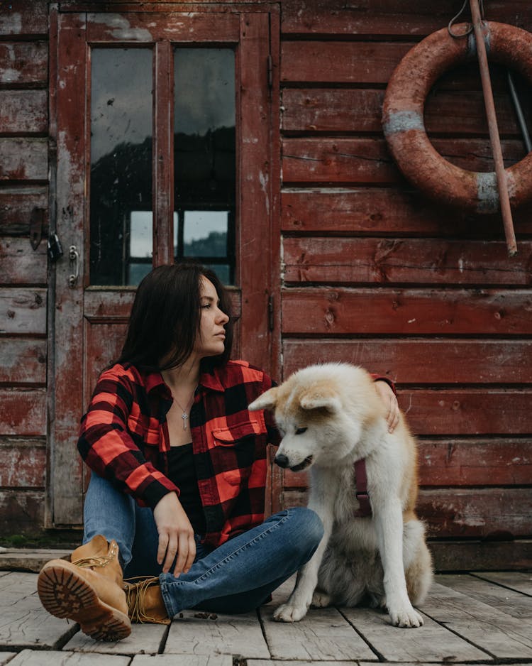 Woman Sitting On Wooden House Porch With Dog