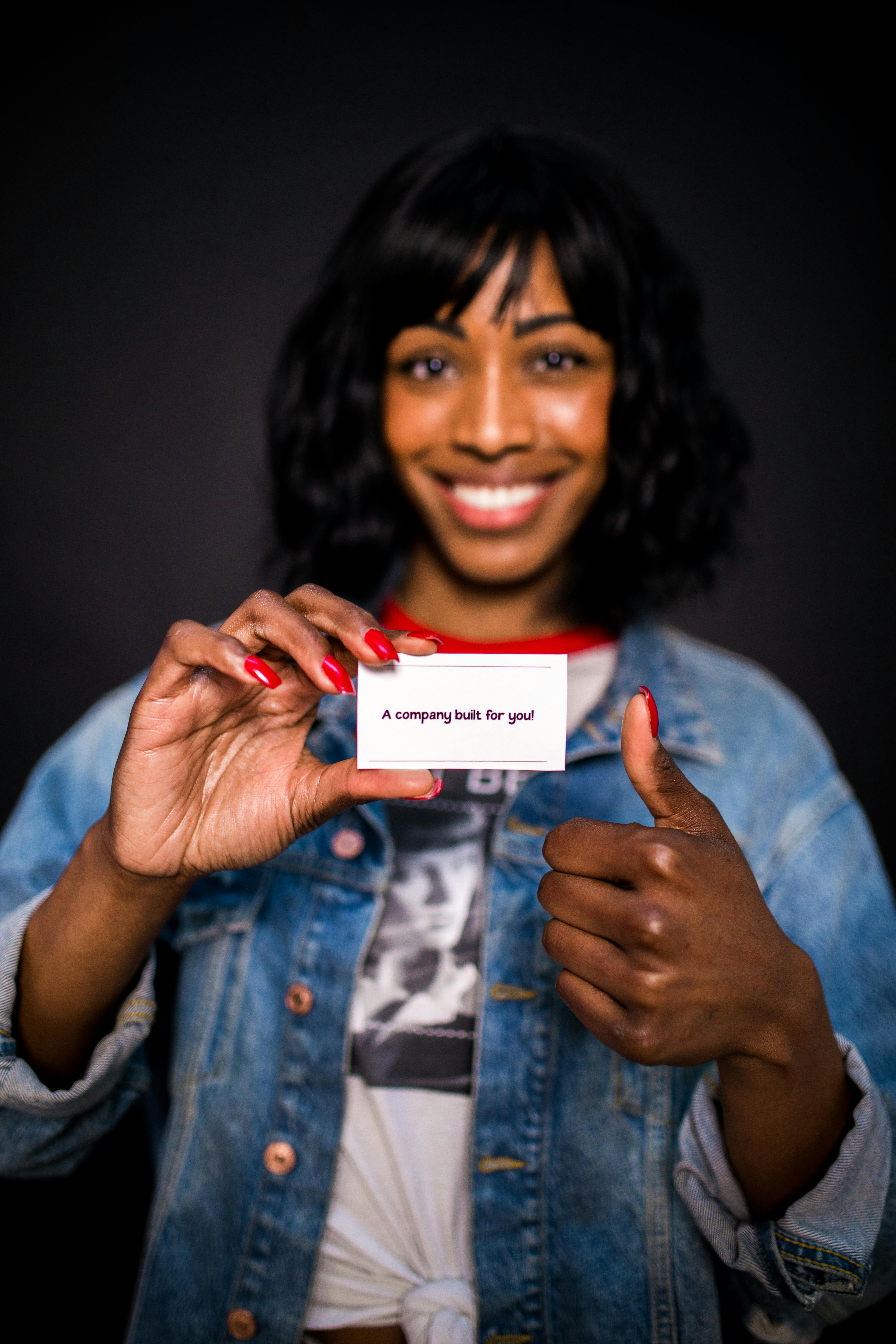 A cheerful woman in a denim jacket presents a business card with confidence.