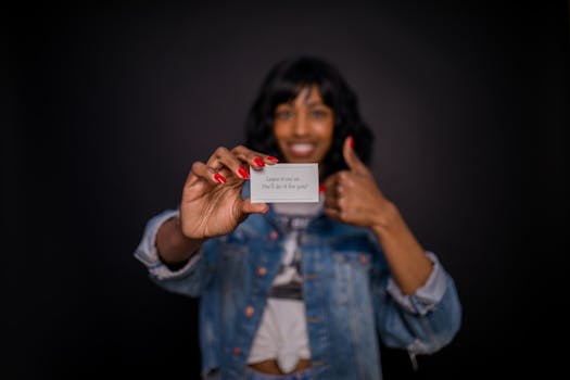 Smiling woman holding a business card with a message in focus, thumbs up sign.