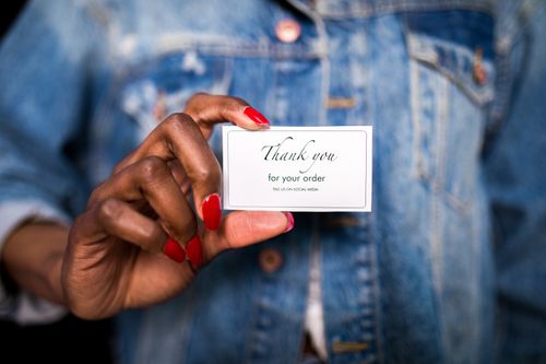 Free A woman in a denim jacket holds a 'Thank You' card with red nails. Stock Photo