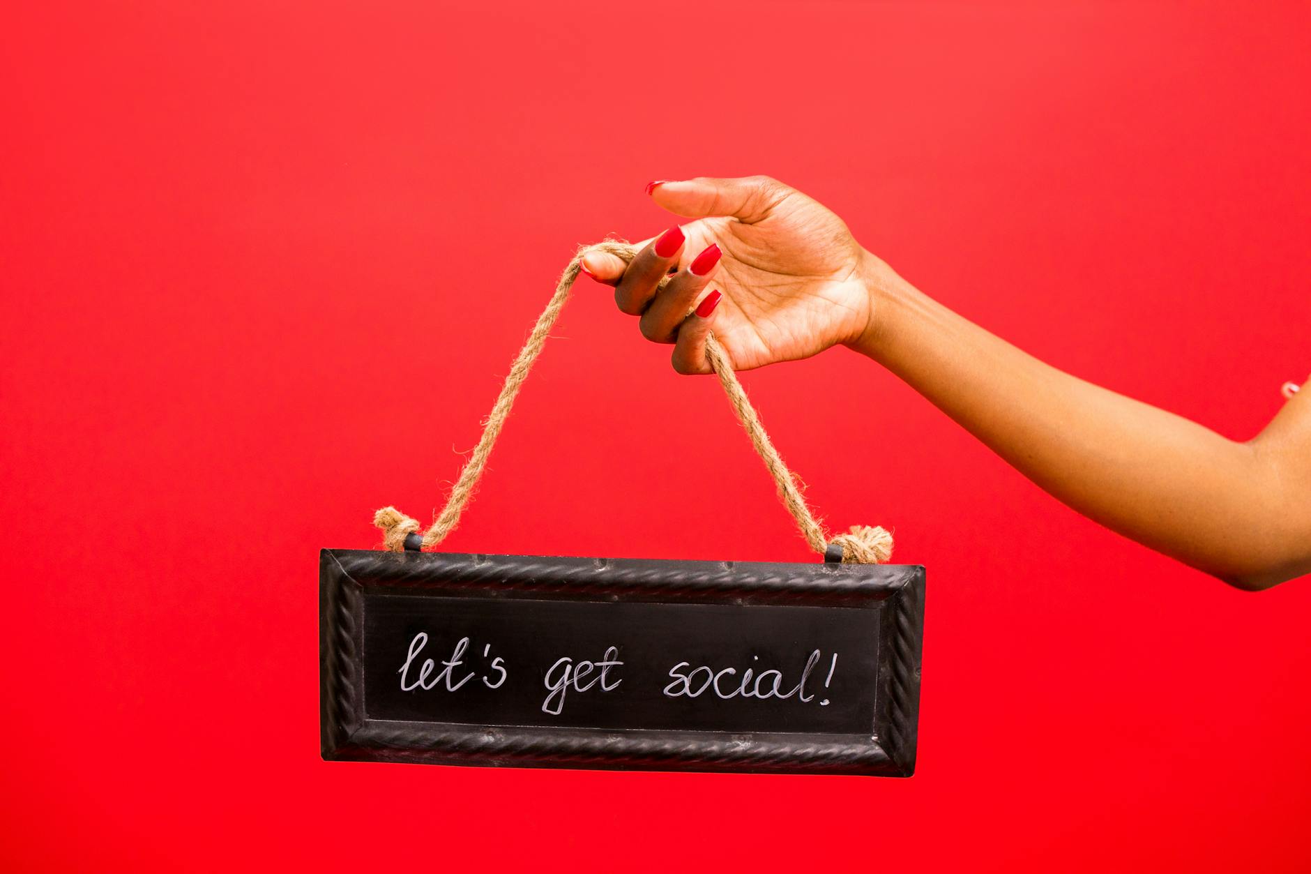 A hand holding a 'Let's Get Social!' sign against a vibrant red background.