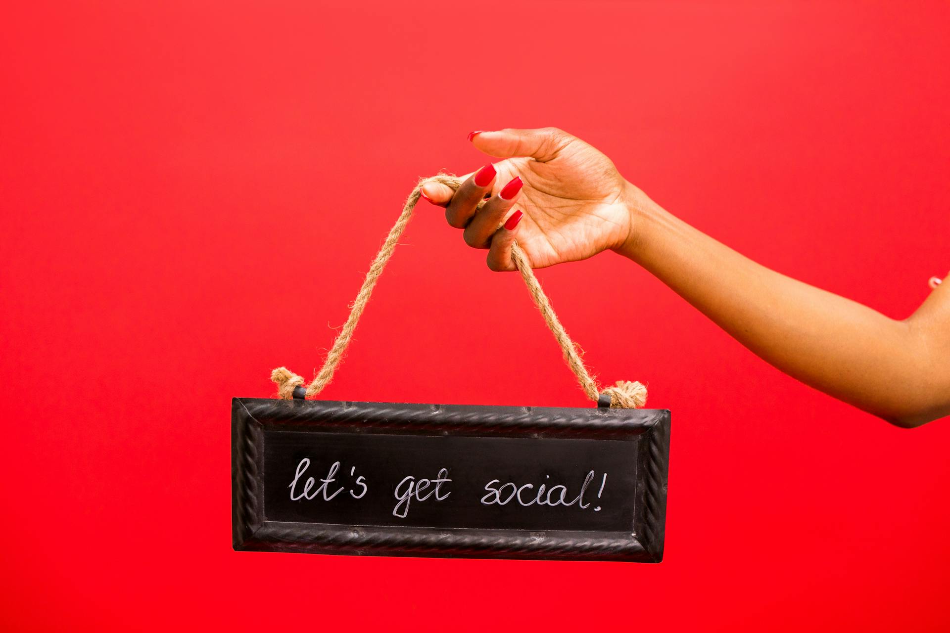 A hand holding a 'Let's Get Social!' sign against a vibrant red background, perfect for online engagement themes.