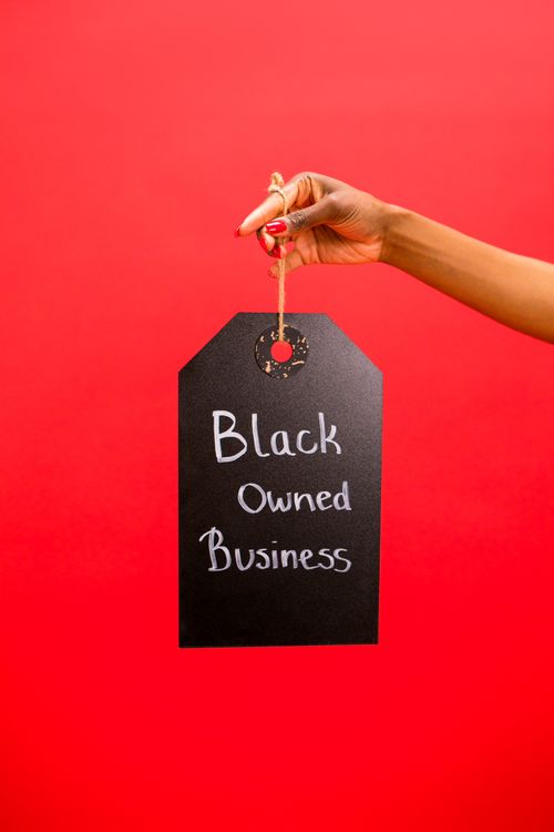 Free A hand holds a black sign with 'Black Owned Business' text against a red background. Stock Photo