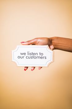 A hand holding a sign saying 'we listen to our customers' on a neutral background.