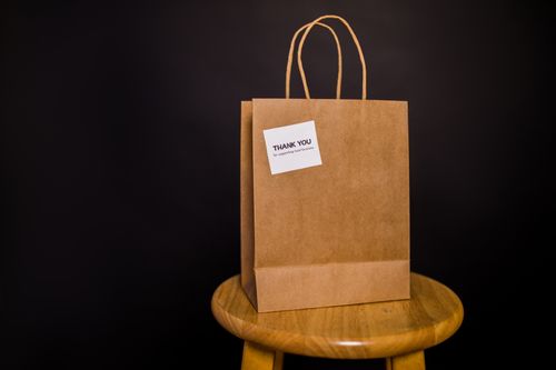Free Brown paper bag with thank you note placed on a wooden stool against a black background. Stock Photo