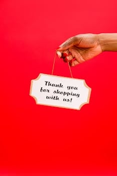 A hand holding a thank you sign on a vibrant red background, conveying gratitude.