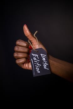 Close-up of a hand with a limited edition tag, thumbs up gesture against dark background.