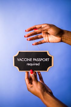 Close-up of hands holding a sign against a blue background reading 'Vaccine Passport Required'.
