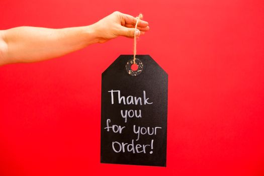 A hand holding a thank you sign for orders against a bold red background.