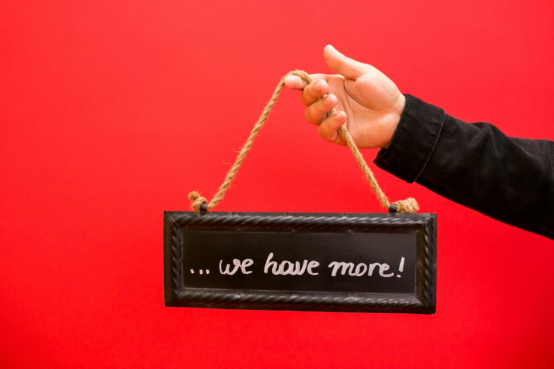 A hand holding a black chalkboard sign with text on a vibrant red background.