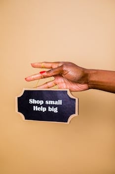 Female hand holds sign with 'Shop small, Help big' message, advocating for small business support.