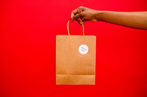 Free A hand holding a paper gift bag labeled 'Special Gift' against a vibrant red background. Stock Photo